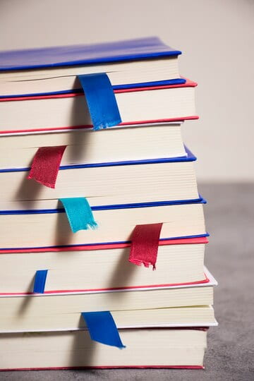 A stack of books with blue and red bookmarks inserted in them.