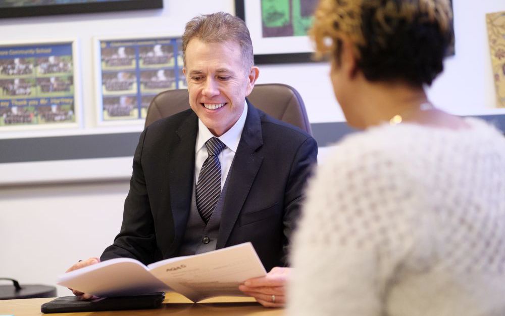 Man wearing smart suit smiles while consulting a booklet.