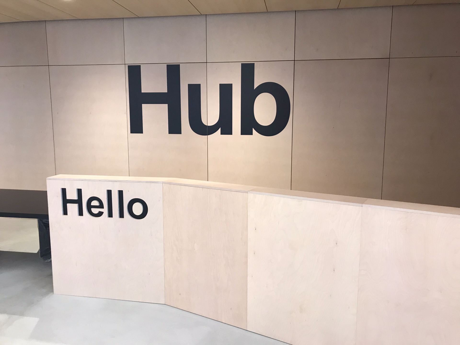 Wooden helpdesk with "Hello" carved in the front of the desk, Hub in big black letters on the wall behind the desk