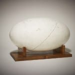 Photo shows a large white egg shaped object on a wooden stand.