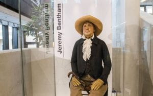 Jeremy Bentham's Auto-Icon with a waxwork head, dressed in his original 19th century clothes, sitting on a wooden chair inside a glass museum display case
