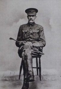 Black and white image of Charles Stoneham in military uniform sitting on a wooden chair holding a riding crop
