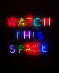 A neon colourful sign that says 'Watch this Space'