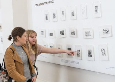 Image of two students pointing to their work on display at the Make an Impression Exhibition launch.