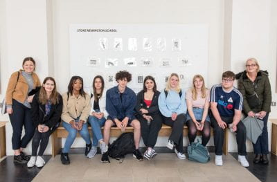 Image of students posing in front of their prints on display for the Make an Impression exhibition in the North Cloisters