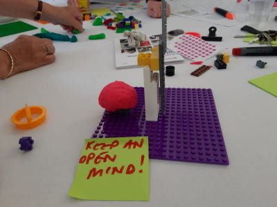 Our table's artwork: a post-it says "keep an open mind!" in front of an artwork that shows a brain made of Play-Doh with a Lego door next to it.