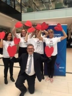 A group of people holding heart decorations. Simon is the one kneeling down!