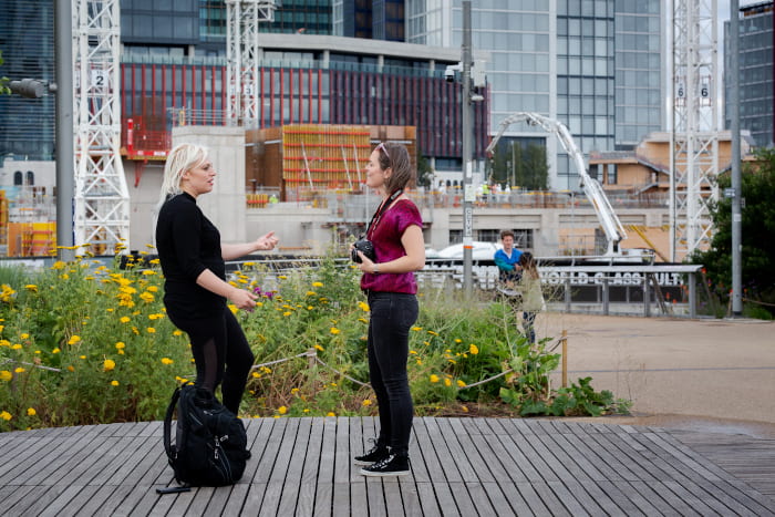 Two women viewed side on speaking, with large construction work behind them