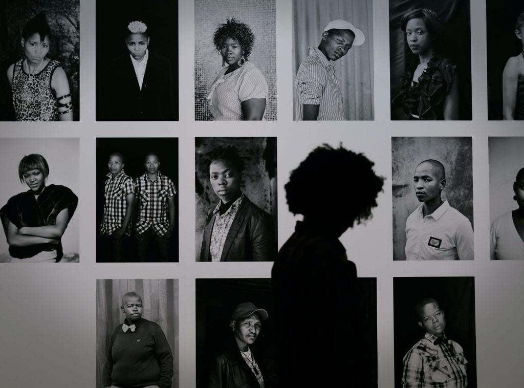 Collage of photographs of a diverse group of black people with a person walking past and looking at it