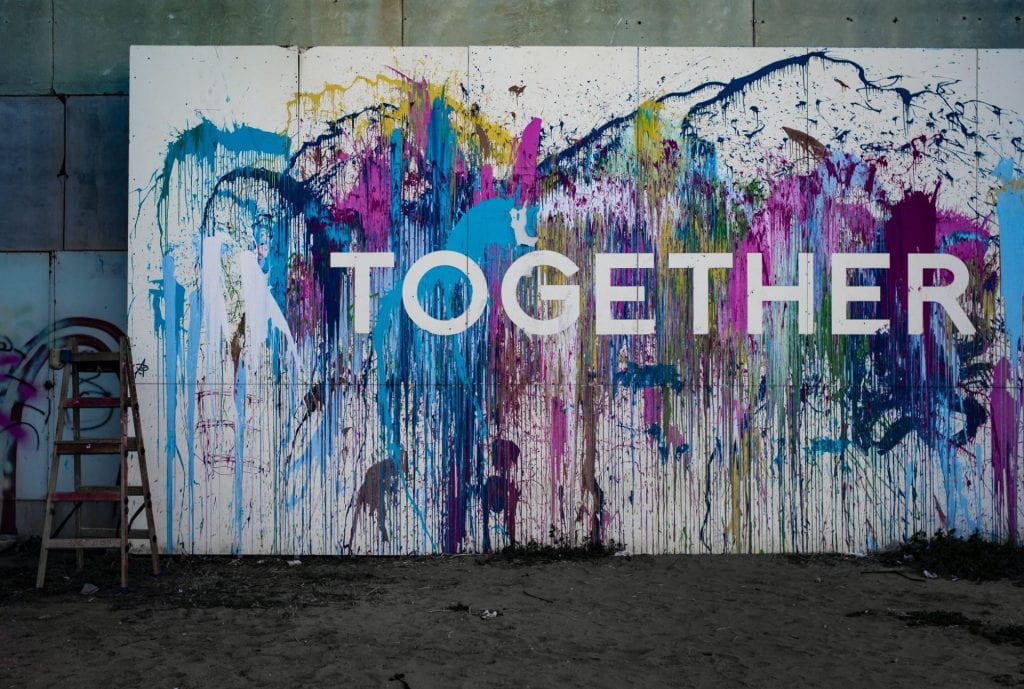 A white wall with multi colours splashed on it and the word 'TOGETHER' in white