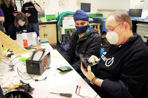 A volunteer from the Restart Project takes apart a broken radio while the owner looks on.