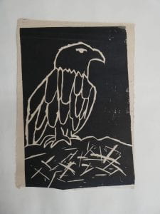 A black and white lino cut print of the profile of an eagle, standing a the edge of its nest.