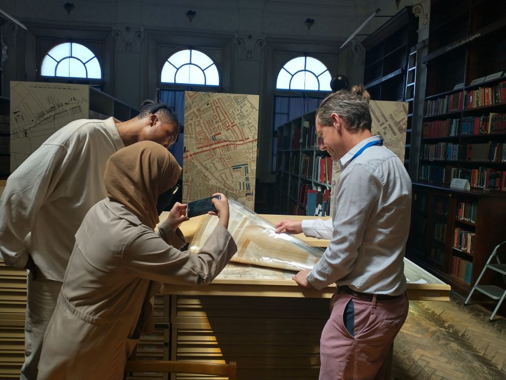 Two young adults and an archivist look at an historical map together in grand surroundings.