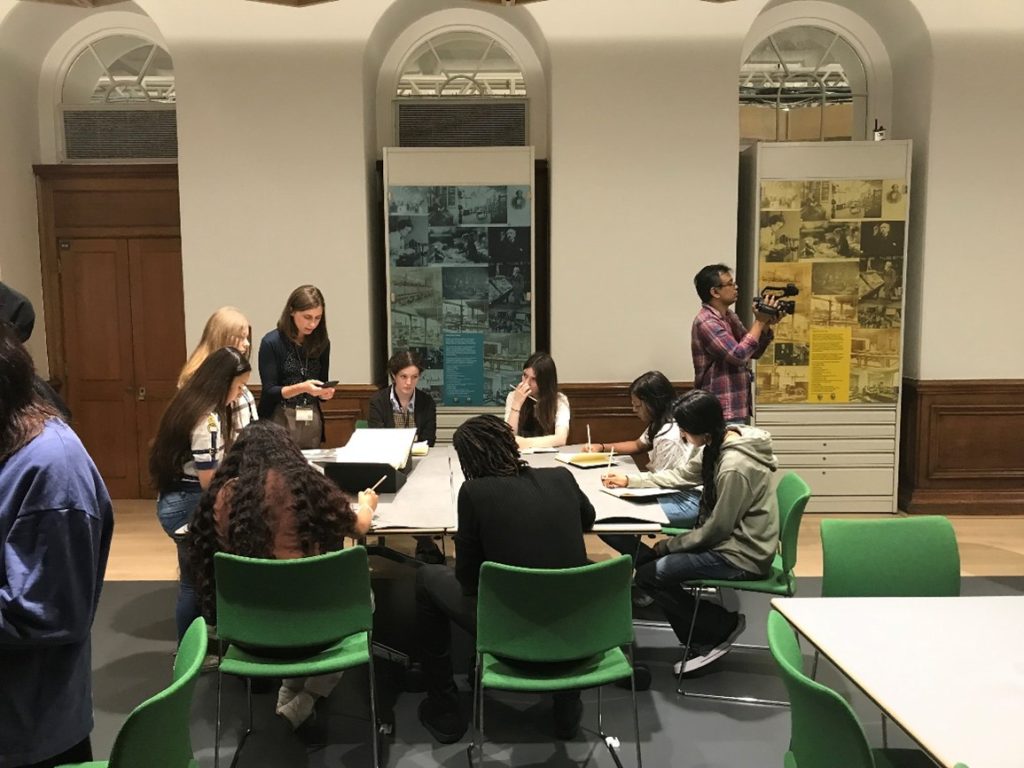 A group of sixth form students sit at a table looking at a manuscript from Special Collections.