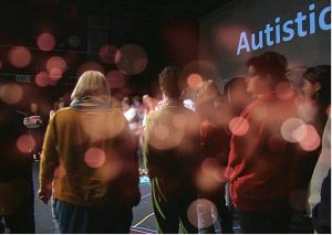 Autie gang group picture: a group of audience members standing on a stage in a semi-circle, with a PowerPoint slide behind them which reads “Autistic”